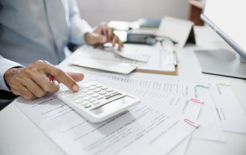 Contabil calculând TVA la încasare pe calculator, analizând facturi și documente financiare ale companiei