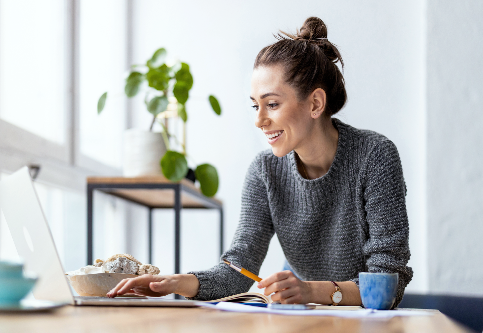 Antreprenoare zâmbind lucrând pe laptop și luând notițe acasă, ilustrând procesul simplu de scontare în 3 pași: creare cont, trimitere cerere de scontare și primirea banilor în cont imediat